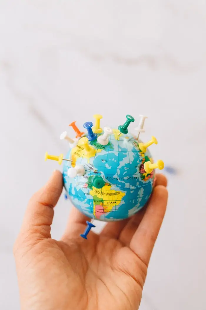 our-services-2 Close-up of a hand holding a mini globe with colorful push pins on a white background.