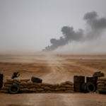Colonnes de fumée s'élevant d'une route désertique dans la Badia syrienne, avec un point de contrôle militaire camouflé au premier plan, symbolisant l'escalade des attaques dans la Jézireh syrienne.