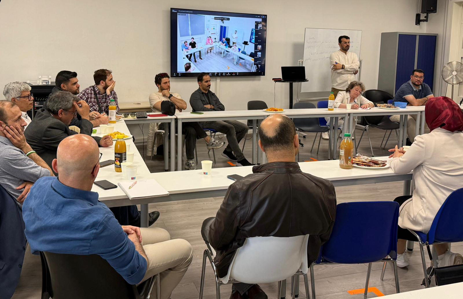 Salle de réunion avec des participants à une rencontre consultative de journalistes et professionnels des médias syriens en France, avec une participation à distance affichée sur un écran