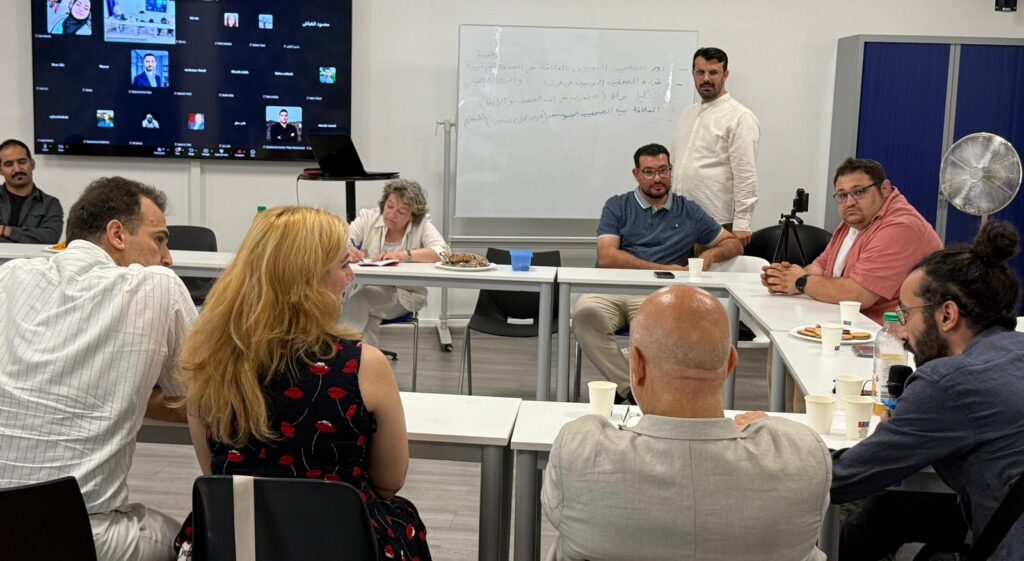 Participants à une rencontre consultative dans une salle de réunion en France, avec un écran affichant une participation à distance via Zoom et un tableau blanc à l’arrière-plan
